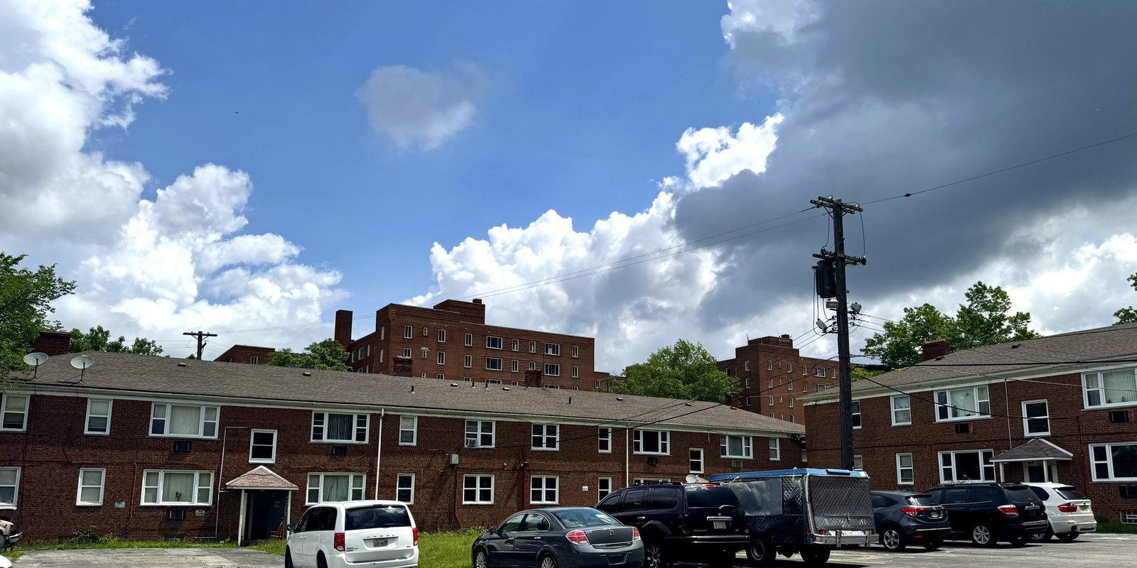 After: a full brick apartment community under a summer sky, residents' cars in the lot
